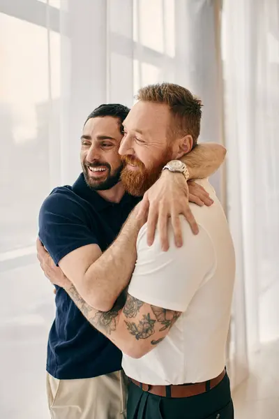 Two men in casual clothes embrace each other warmly in front of a window in a modern living room. — Stock Photo