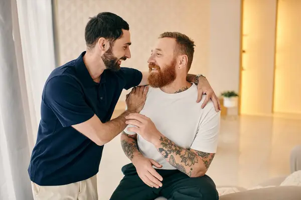 Zwei Männer in lässiger Kleidung umarmen sich in einem modernen Wohnzimmer herzlich und zeigen Zuneigung und Liebe in einem intimen Moment. — Stockfoto