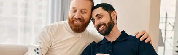 Щаслива гомосексуальна пара в повсякденному одязі, з бородою, ділиться теплими обіймами на зручному дивані в сучасній вітальні. — стокове фото