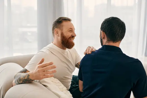 Two men in casual clothes, a happy gay couple, sit on a couch in a modern living room, engaged in a lively conversation. — Stock Photo