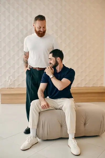 Dois homens, um feliz casal gay, sentam-se ao lado um do outro em uma sala de estar moderna, compartilhando tempo de qualidade juntos. — Fotografia de Stock