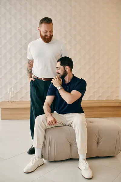 Two men, a happy gay couple, sit next to each other in a modern living room, sharing quality time together. — Stock Photo