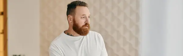 Un homme à la barbe rouge perdu dans la pensée, dans un cadre de salon moderne. — Photo de stock