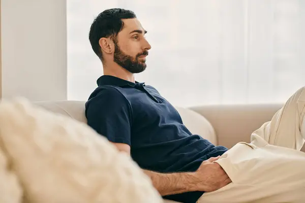 Um homem com barba senta-se confortavelmente em um sofá em uma sala de estar moderna, desfrutando de tempo de qualidade — Fotografia de Stock