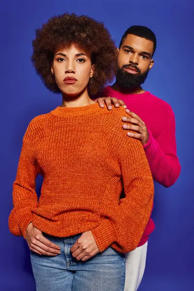 A young African American man and woman, friends, stand together in vibrant casual attire against a blue background. — Stock Photo