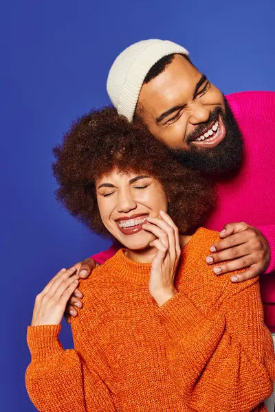 A man and a woman, young African American friends, embrace in a warm hug, displaying the bond of friendship on a blue background. — Stock Photo