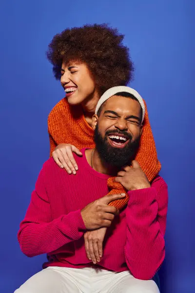 Um homem com barba abraça ternamente uma mulher, seu traje vibrante contrastando com um fundo azul. — Fotografia de Stock