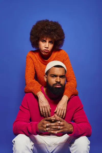 Young African American friends in casual attire, woman sitting atop mans shoulders against a blue background. — Stock Photo
