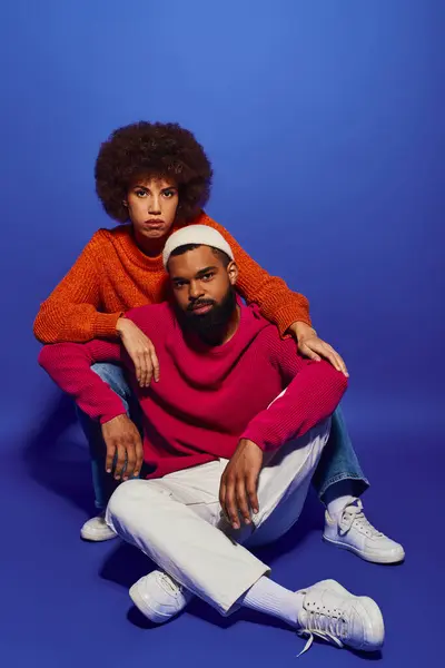 Un giovane uomo e una donna afroamericani, amici in abiti casual vivaci, seduti insieme su uno sfondo blu. — Foto stock