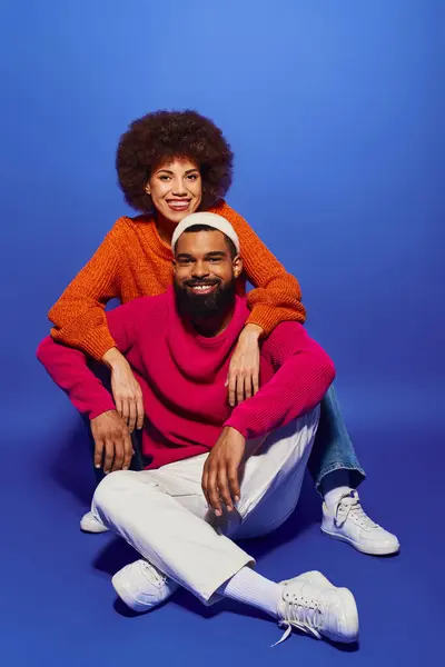 Un jeune homme et une jeune femme afro-américaine en tenue décontractée vibrante assis sur le sol, incarnant l'amitié et la compagnie. — Photo de stock