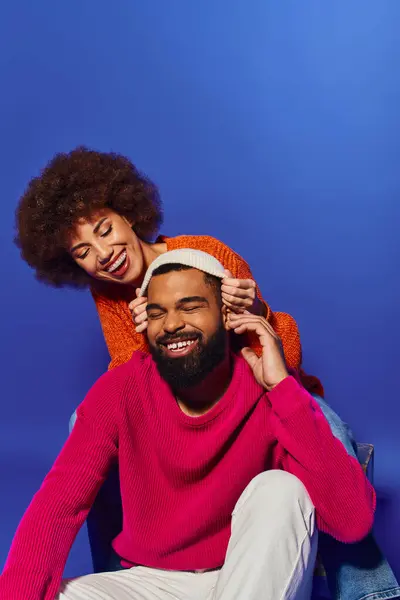 Une jeune femme afro-américaine en tenue vibrante est assise au sommet d'un homme dans une démonstration lumineuse et ludique d'amitié. — Photo de stock