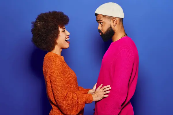 An African American man and woman, friends, stand side by side in vibrant casual attire against a blue background. — Stock Photo