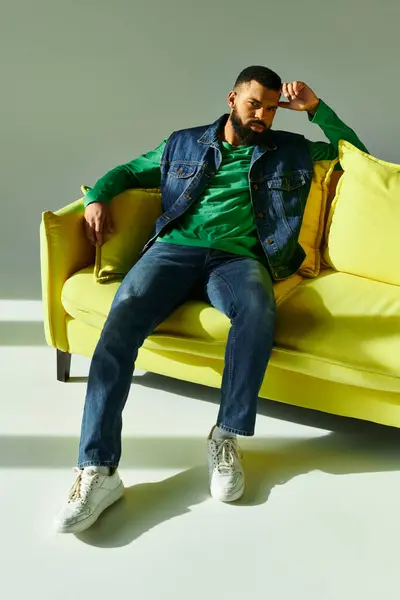 A man confidently sits on a yellow couch against a grey backdrop. — Stock Photo