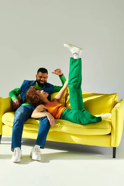 Fröhliche afroamerikanische Freunde in lebendiger Kleidung genießen es, auf einer gelben Couch zu sitzen. — Stockfoto