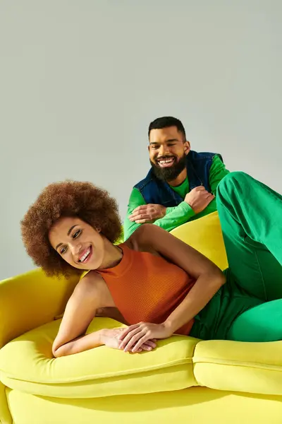 Happy African American friends in vibrant clothes sitting on a yellow couch against a grey background, showcasing friendship. — Stock Photo