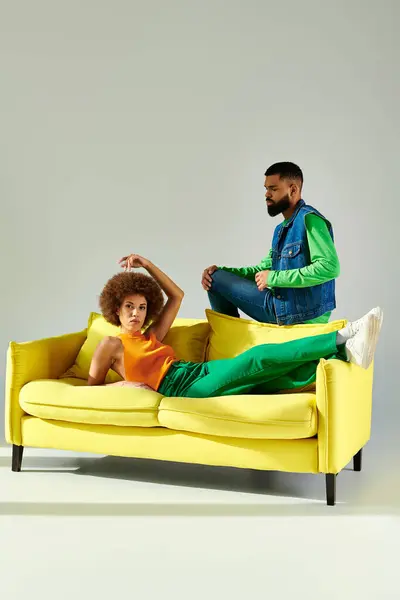 Happy African American friends, man and woman, sitting on a yellow couch in vibrant clothes, showcasing friendship. — Stock Photo