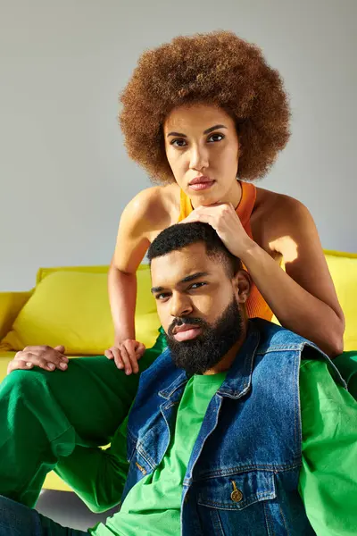 Amigos afroamericanos se sientan en un sofá amarillo, mostrando amistad entre un hombre y una mujer en ropa vibrante. - foto de stock