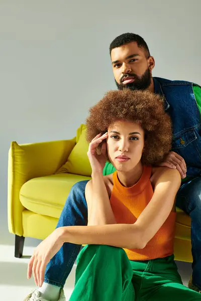 Happy African American friends in vibrant clothes sit together on a yellow couch against a grey background. — Stock Photo