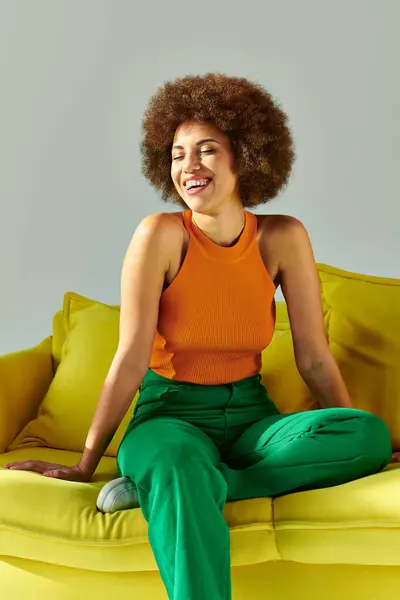 An African American woman in vibrant clothes sits atop a yellow couch — Stock Photo