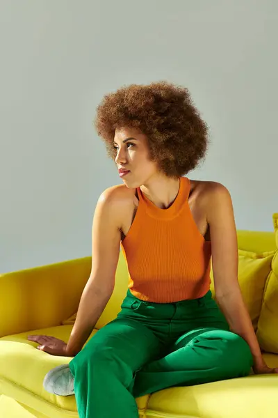 Une femme afro-américaine s'assoit gracieusement sur un canapé jaune, incarnant sérénité et dynamisme dans son environnement. — Photo de stock