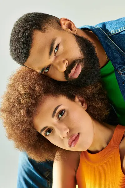 An African American man and woman, in colorful outfits, pose for a picture while sitting on a yellow couch against a grey backdrop. — Stock Photo