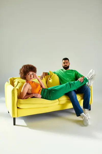 Afroamerikanische Freunde sitzen fröhlich auf der gelben Couch und zeigen in lebendiger Kleidung Freundschaft und Verbundenheit. — Stockfoto