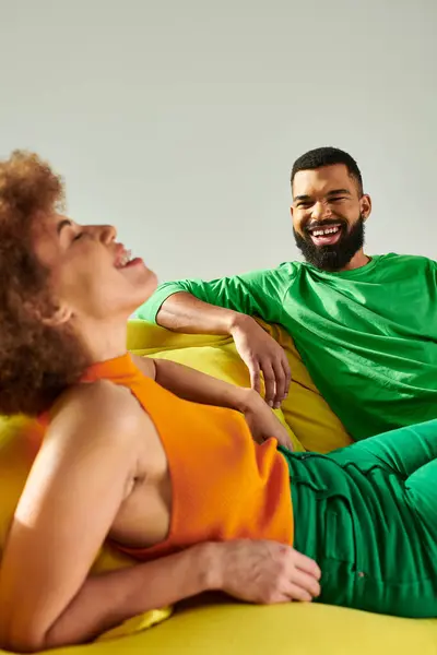 A man and a woman, happy African American friends, reclining on a bean bag chair in vibrant clothes, symbolizing friendship. — Stock Photo