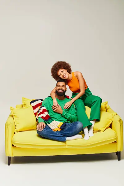 Smiling African American friends in colorful attire relaxing on bright yellow couch against a grey backdrop, showcasing connectivity and friendship. — Stock Photo