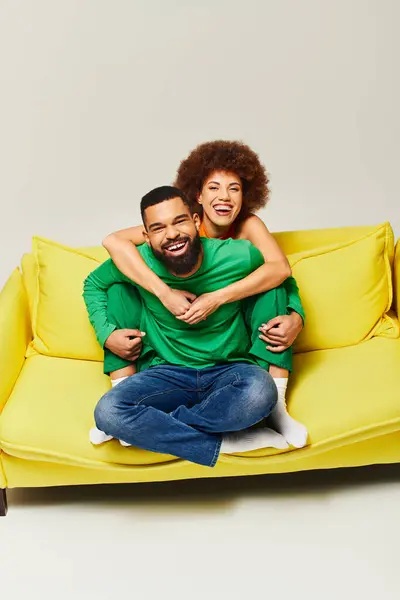 Happy African American friends in vibrant clothes sit on a yellow couch, showcasing the friendship between a man and a woman. — Stock Photo