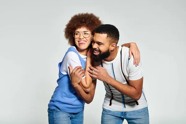 An African American couple in stylish clothes share a warm hug, expressing their deep friendship against a grey background. — Stock Photo