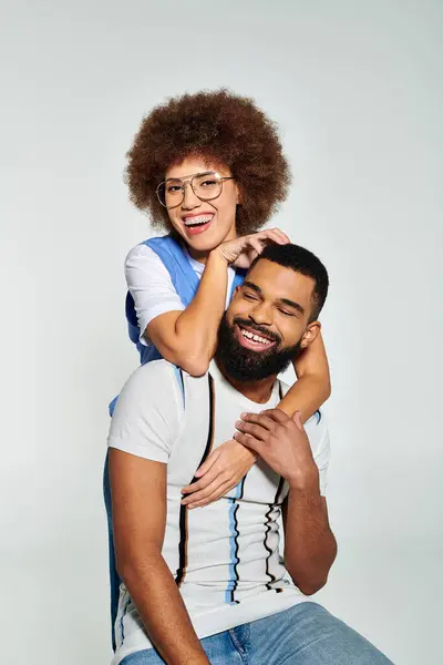 An African American man holds a woman on his shoulders, showcasing strength and friendship in stylish clothes on a grey background. — Stock Photo