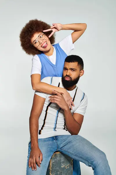 An African American man and woman in stylish clothes sitting together against a grey background. — Stock Photo