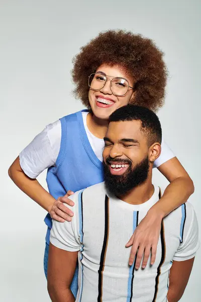 An African American man with beard and glasses embraces a woman in stylish clothes against a grey background. — Stock Photo