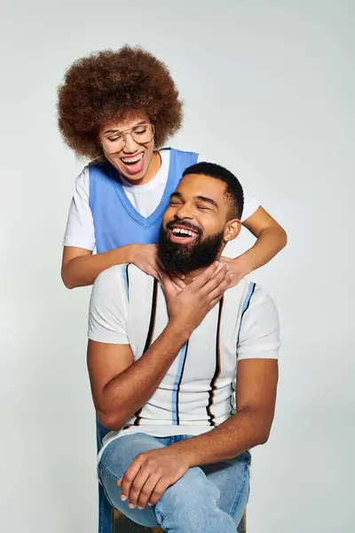 African American friends in stylish clothes showcase friendship as man holds woman on his shoulders against a grey background. — Stock Photo