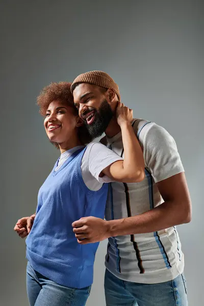 Amigos afroamericanos, con un atuendo elegante, compartiendo un cálido abrazo contra un fondo gris, celebrando su amistad. - foto de stock