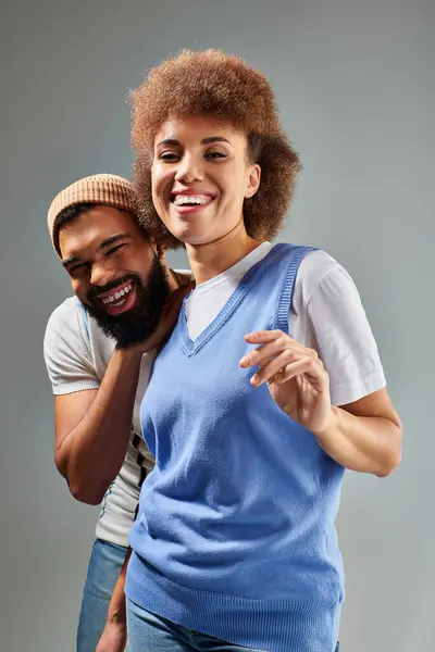 Un homme et une femme afro-américains dans des vêtements élégants riant ensemble, montrant leur forte amitié sur un fond gris. — Photo de stock