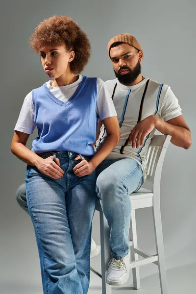 African American man and woman in stylish clothes sitting on chair, showcasing friendship on grey background. — Stock Photo