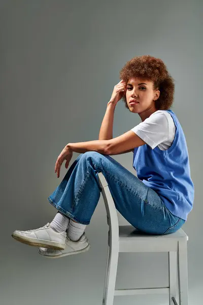 A woman of color elegantly seated on a pristine white chair, exuding grace and poise against a neutral backdrop. — Stock Photo