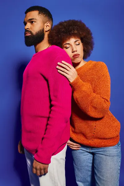A young African American man and woman, friends in vibrant casual attire, standing together on a blue background. — Stock Photo