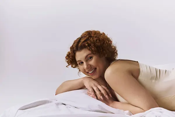 A young curvy redhead woman laying on a bed, smiling contentedly. — стоковое фото