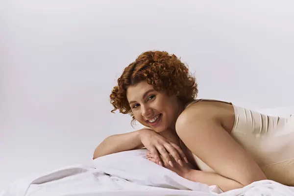 A young curvy redhead woman laying on a bed, smiling contentedly. — Stock Photo