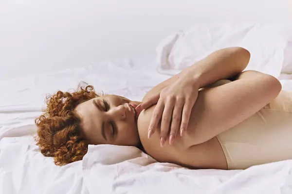 Curvy redhead woman in lingerie lying on bed with crossed arms. — Foto stock