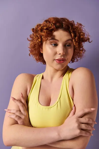 A young, curvy redhead woman in a yellow top striking a confident pose with her arms crossed. — Stockfoto
