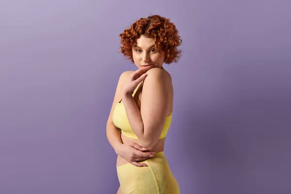 Curvy redhead in yellow bikini strikes a pose against a vibrant purple backdrop. — Photo de stock