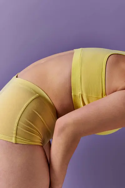 A young, curvy redhead woman in a yellow bikini gracefully performs a yoga pose on a vibrant purple background. — стокове фото