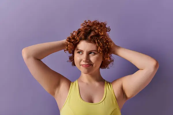 A young woman with curly red hair striking a pose in yellow underwear against a bold purple backdrop. — Fotografia de Stock