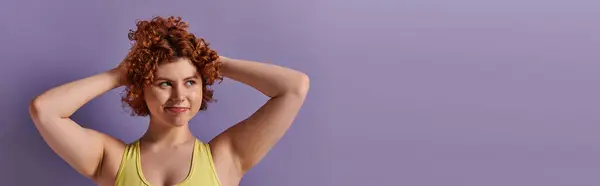 A young, curvy redhead woman in yellow underwear striking a pose against a vibrant purple background. — Stock Photo