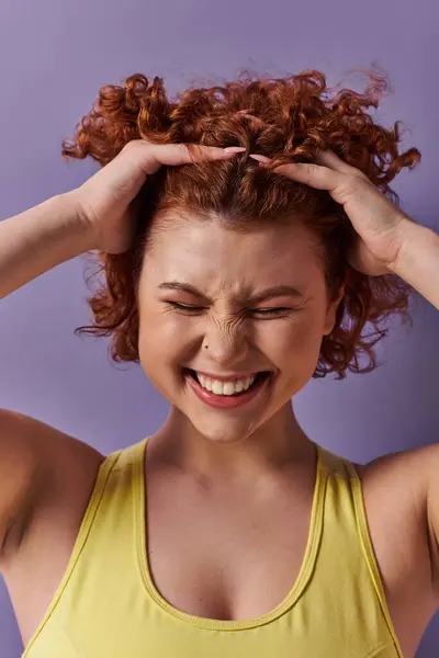 A young, curvy redhead woman in yellow underwear is holding her head in her hands on a purple background. — Stockfoto