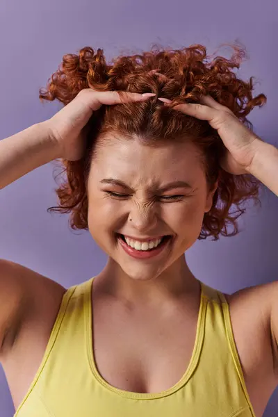 A young, curvy redhead woman in yellow underwear is holding her head in her hands on a purple background. — Stock Photo