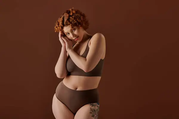 Young, curvy redhead woman exudes confidence in brown bikini on brown background. — Stockfoto
